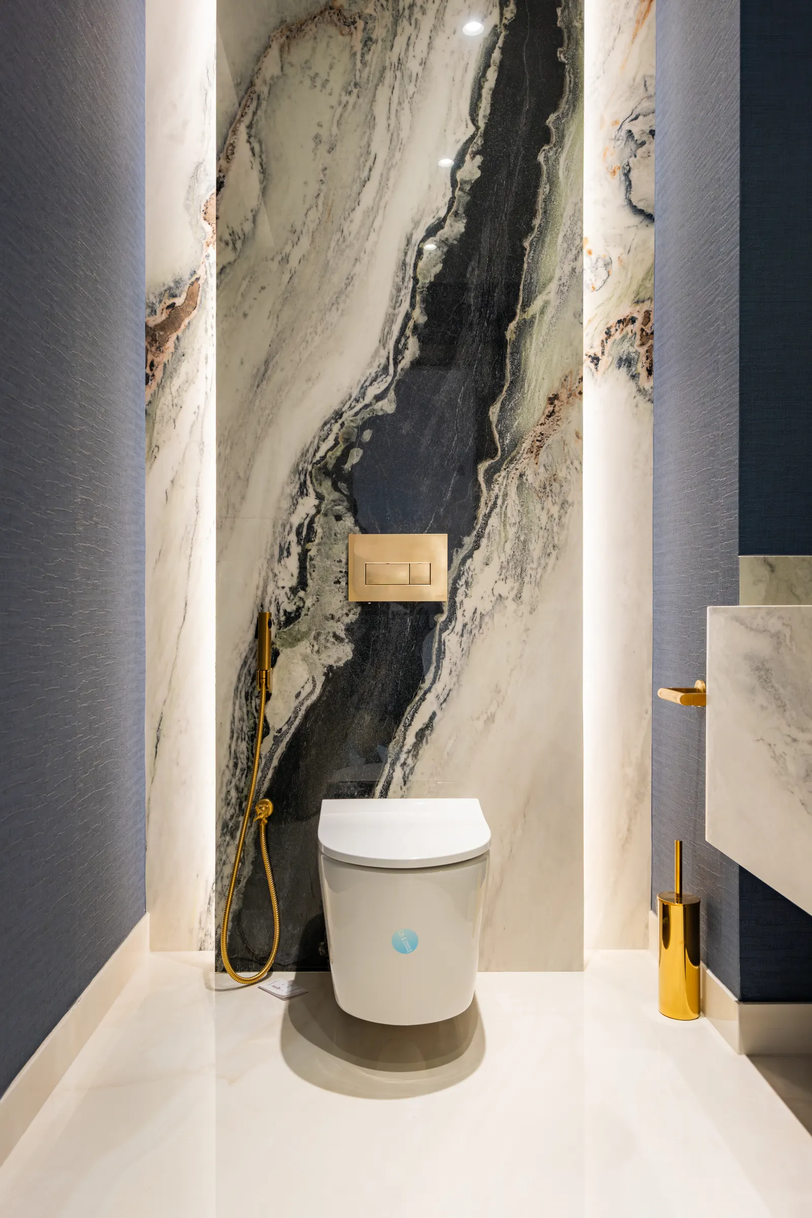 Twyst Interiors.Barsha Villa powder room with dramatic veined marble feature wall, deep navy walls, brushed gold fittings.