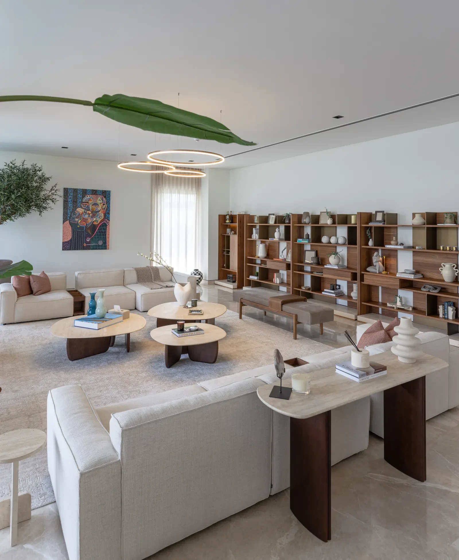 Twyst Interiors.Golf Place open-plan living room with travertine surfaces, gallery shelving, palm leaves overhead. Calm and considered.
