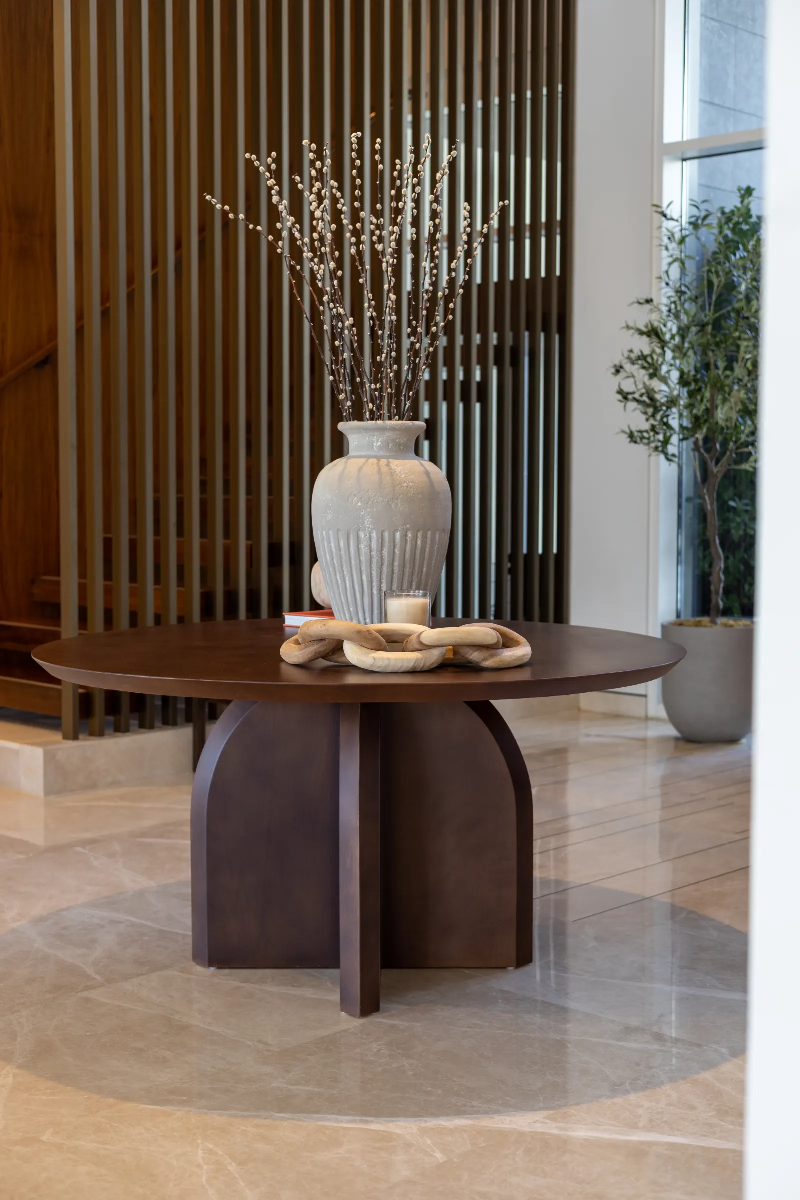 Twyst Interiors.Dubai Hills GP open-plan living room with cream sofas, travertine tables, banana leaf overhead.