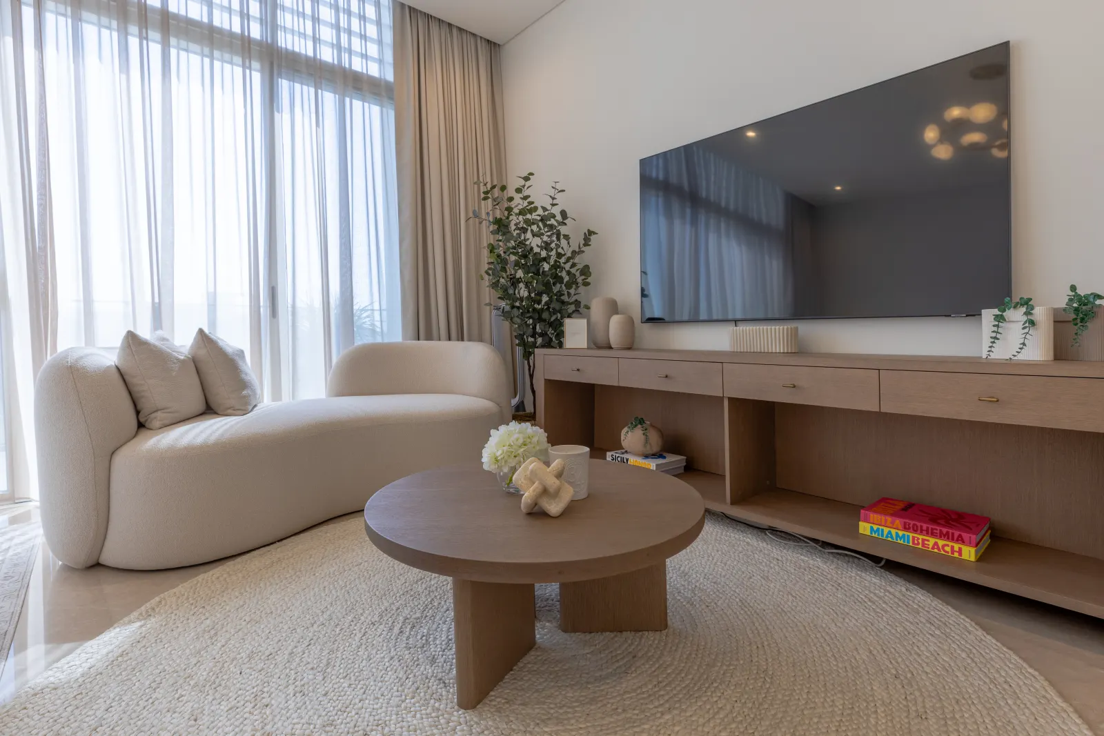 Dubai Hills villa living room. Boucle daybed, sculpted oak coffee table, full-height curtain wall to the garden.