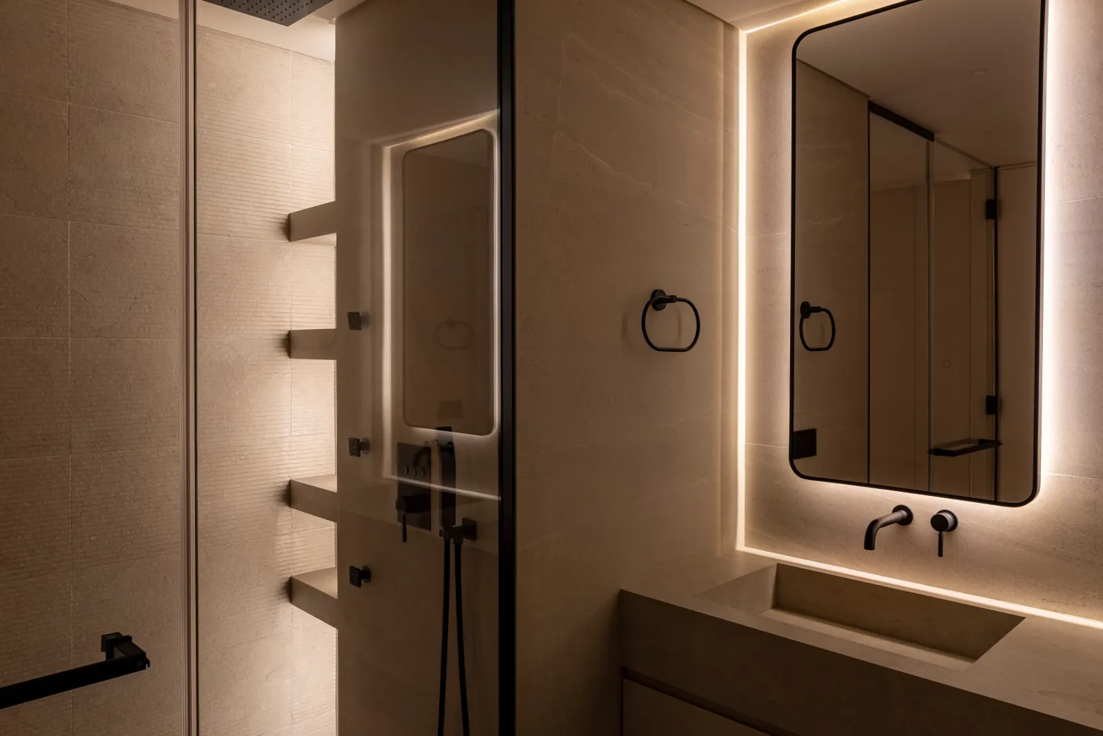 Twyst Interiors.Turk Villa primary bathroom with twin backlit mirrors, warm stone vanity, brushed black fittings.