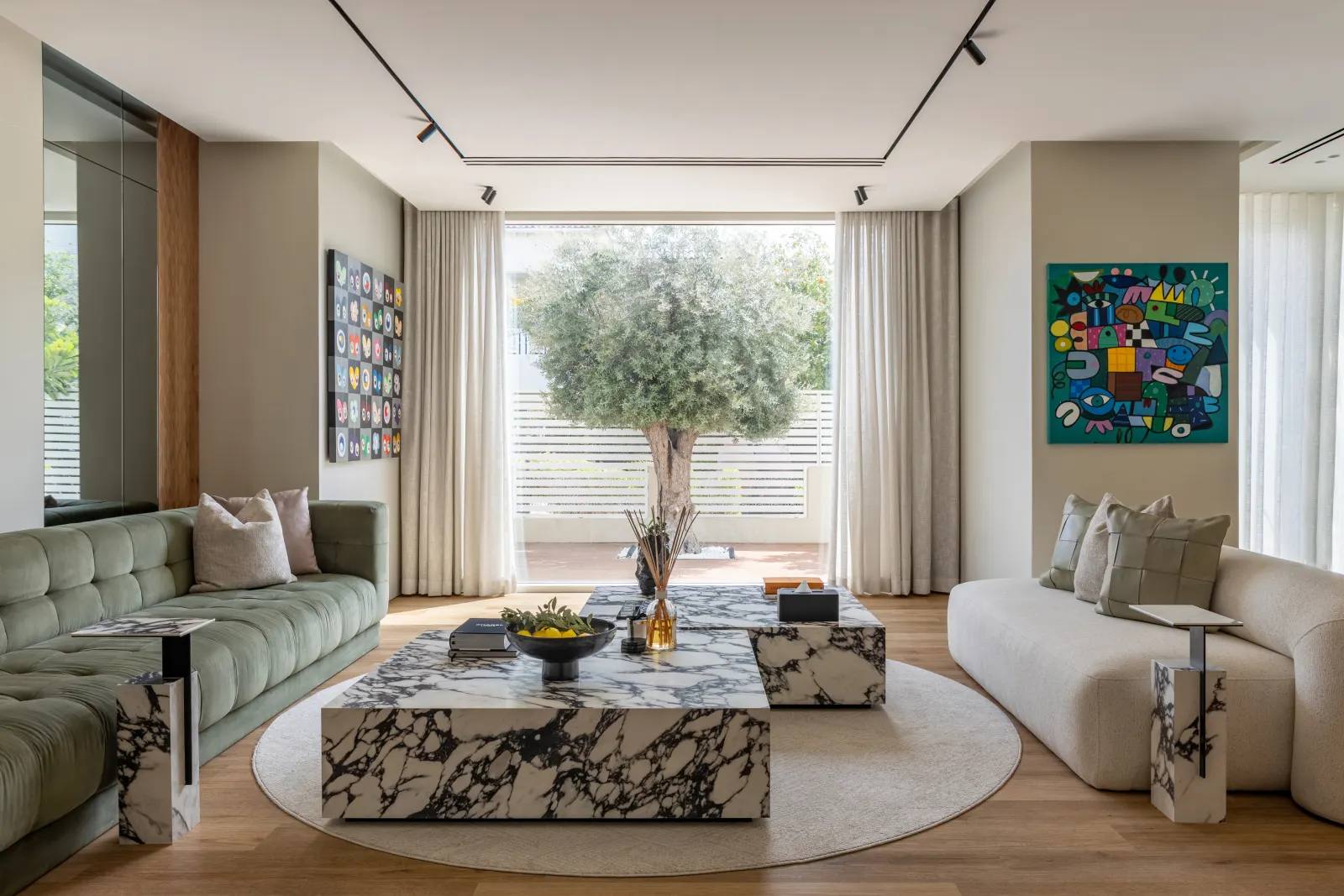 Turk Villa living room. Marble coffee block, olive tree centerpiece, layered green sofas, mirrored art on both walls.