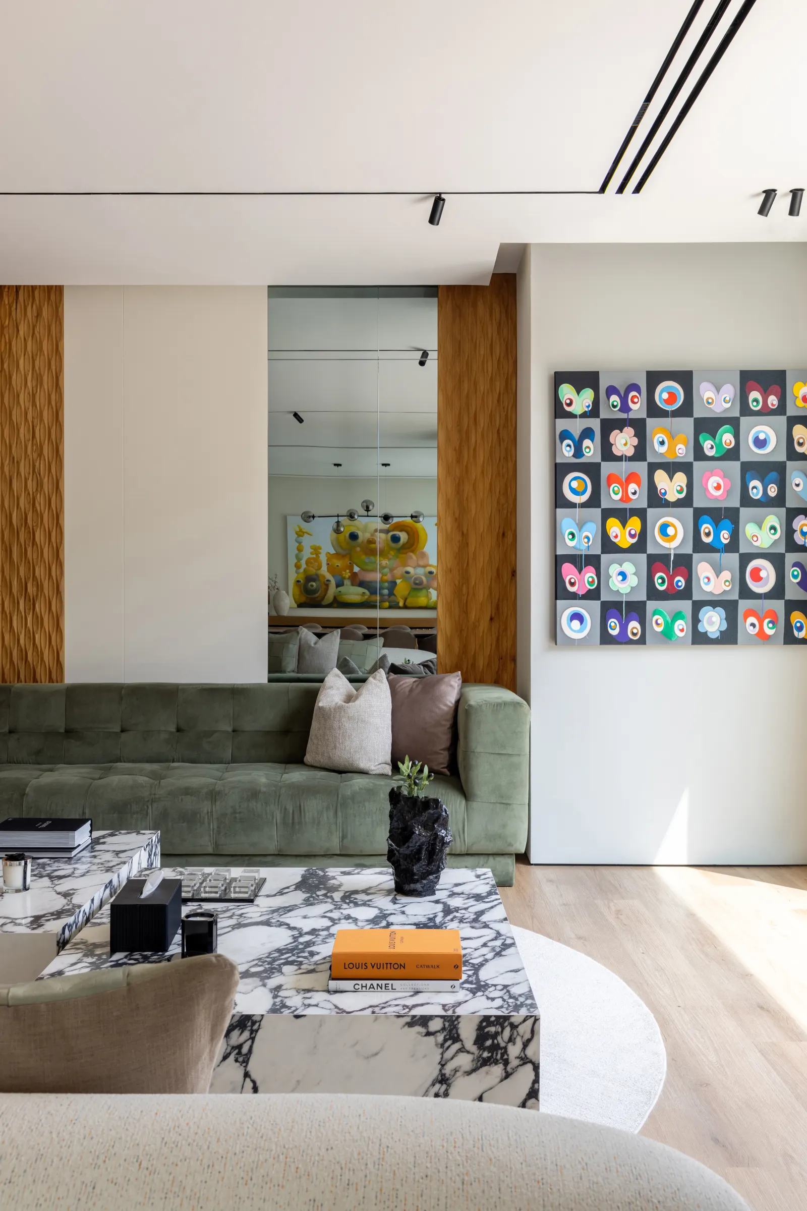 Twyst Interiors. Turk Villa living room corner with sage velvet sofa, fluted walnut wall, layered art grid, marble coffee tables. Custom joinery and material coordination decided in the studio long before the wall went up.